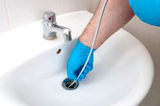 plumber unclogging bathroom drain with drain snake