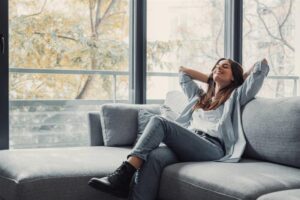 Woman relaxing comfortably on a couch in a cozy, well-humidified home, enjoying balanced indoor air quality near large windows. 