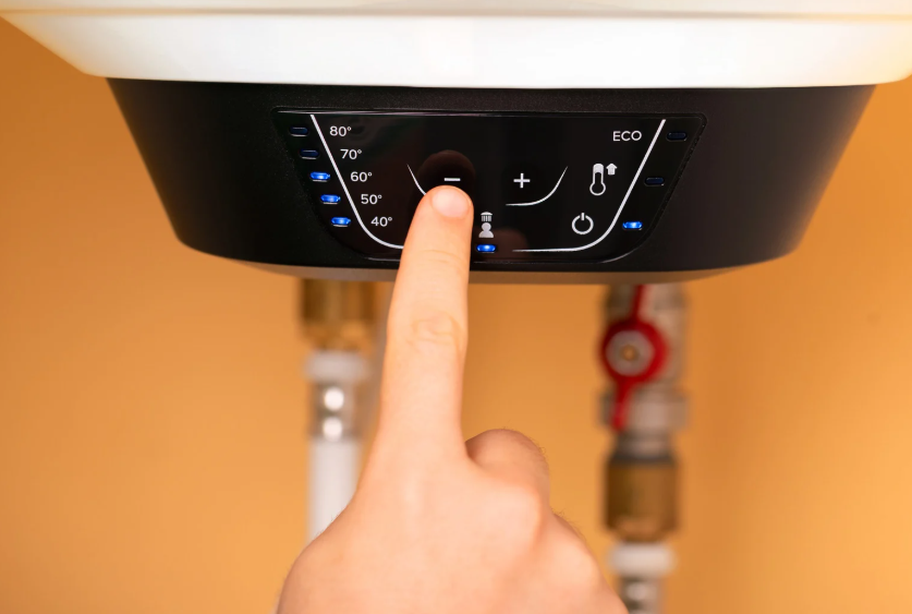 Close-up of a finger pressing a button on a digital water heater control panel, adjusting the temperature setting.