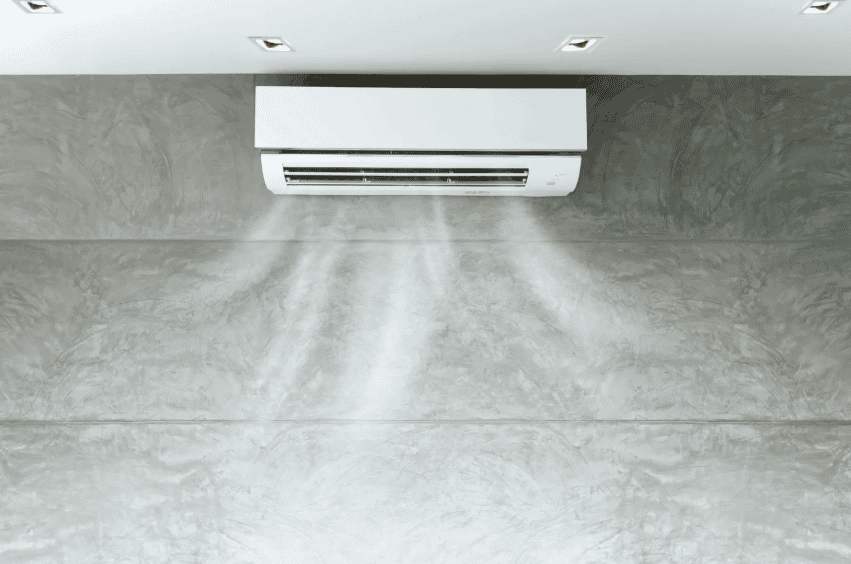Wall-mounted air conditioner blowing cool air into a modern, grey-toned room with recessed ceiling lights.