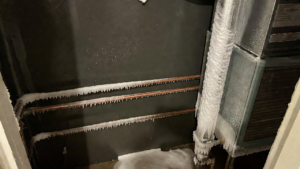 %Focuskw% | Grapids Home Services Frozen pipes and HVAC system components covered in thick ice and frost, with ice buildup on the floor and walls in a utility room.