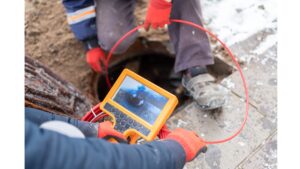 %Focuskw% | Grapids Home Services Two workers use a video inspection camera to examine the inside of a pipe or sewer through an open manhole outdoors in cold weather.